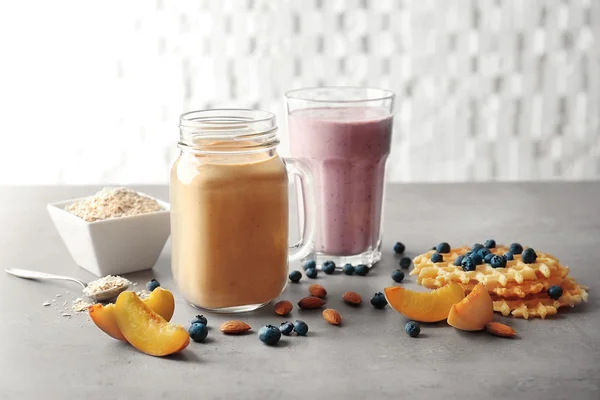 Mason jar och glas med läckra smoothies, wafer och vissa ingredienser på köksbordet — Stockfoto