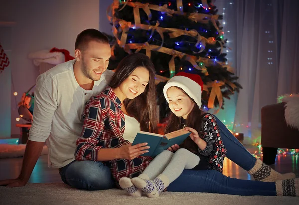 Niña y su familia leyendo el libro en la sala de estar decorado para la Navidad —  Fotos de Stock