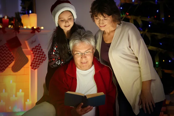 Dziewczynka i jej dziadków, czytanie książki w salon urządzony na Boże Narodzenie — Zdjęcie stockowe