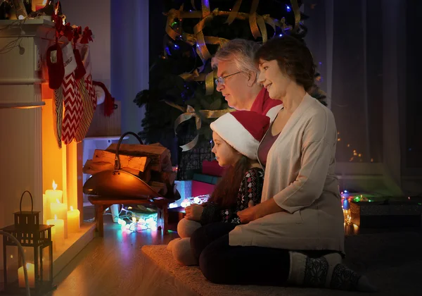Klein meisje en haar grootouders in de buurt van open haard versierd voor de kerst — Stockfoto