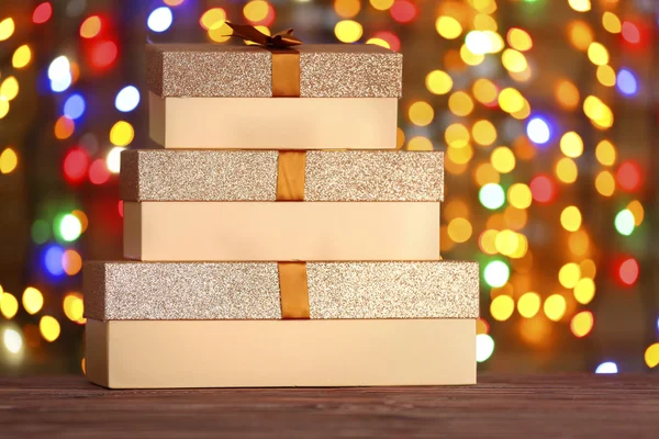 Vakken met Kerst presenteert op houten oppervlak tegen intreepupil lichten — Stockfoto