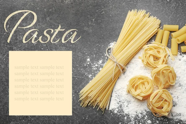 Different pasta with flour on gray table. Italian food concept. Word PASTA on background. — Stock Photo, Image