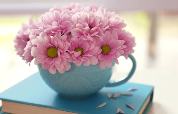 Boeket van mooie bloemen in een kopje op een boek — Stockfoto