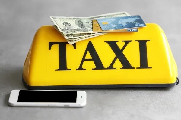Желтый знак крыши такси с телефоном, кредитными картами и американскими долларами на сером фоне, крупный план — стоковое фото