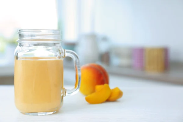 Jug with tasty smoothie and peach on kitchen table — Stock Photo, Image