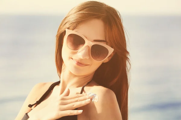 Young woman in sunglasses applying sunscreen on shoulder. Skin care concept. — Stock Photo, Image