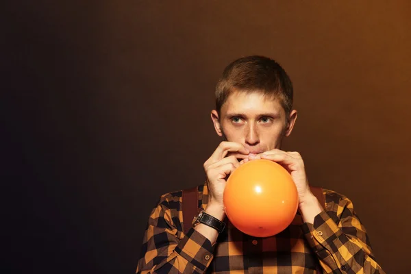 Young man puffing balloon on dark background — Stock Photo, Image