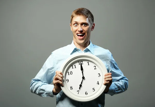 Young man in shirt holding clock on grey background — Stock Photo, Image