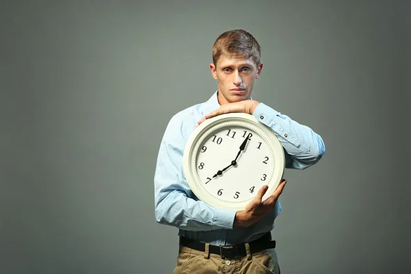 Молодой человек в рубашке держит часы на сером фоне — стоковое фото