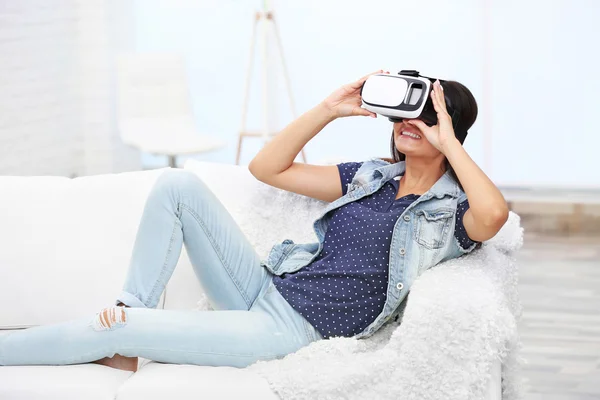 Młoda kobieta nosi okulary wirtualnej rzeczywistości na kanapie w pokoju — Zdjęcie stockowe