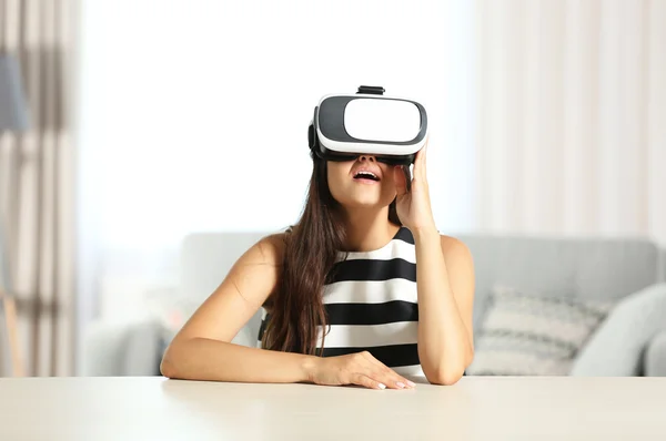Młoda kobieta sobie okulary wirtualnej rzeczywistości i siedzi na kanapie przy stole — Zdjęcie stockowe