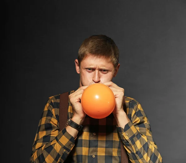 Young man puffing balloon on dark background — Stock Photo, Image