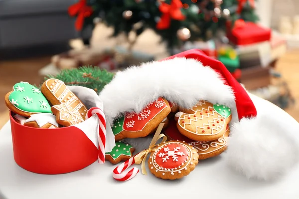 Schachtel mit Lebkuchen und Weihnachtsmann-Mütze auf weißem Tisch vor verschwommenem Hintergrund — Stockfoto