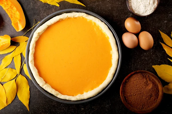 Ongebakken pompoen taart in ovenschaal op donkere achtergrond — Stockfoto