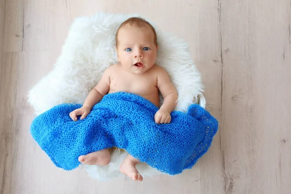 Niedliches Baby auf weißem, flauschigem Plaid liegend und mit blauer Decke bedeckt — Stockfoto