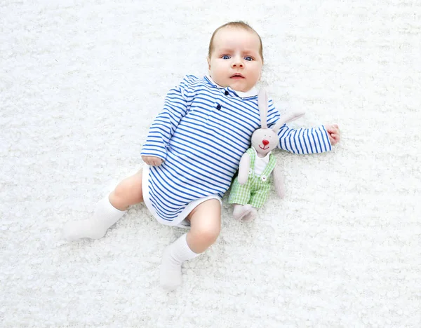 Carino bambino con coniglio coccoloso sdraiato sul copriletto bianco — Foto Stock