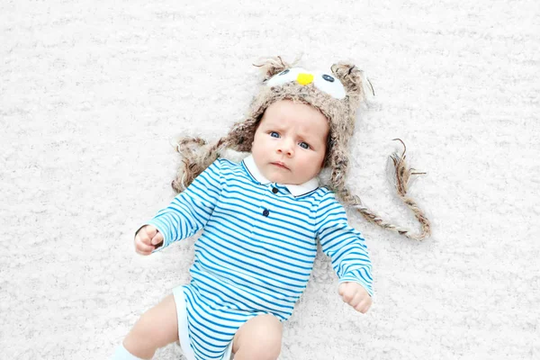 Bambino carino con divertente berretto a maglia sdraiato sul copriletto bianco, vista da vicino — Foto Stock