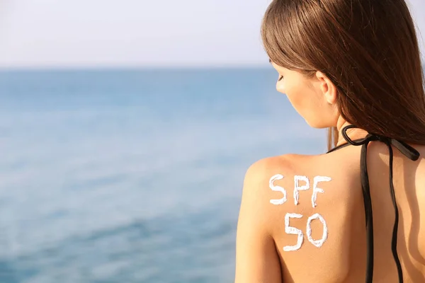 Mladá žena s opalovací krém na zádech, moře pozadí — Stock fotografie