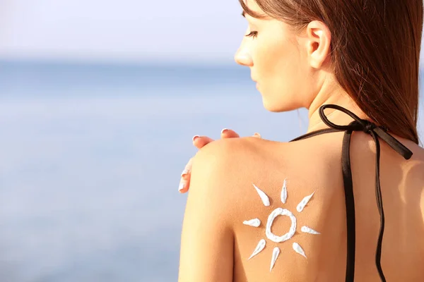 Mujer joven con protector solar en la espalda, fondo marino —  Fotos de Stock