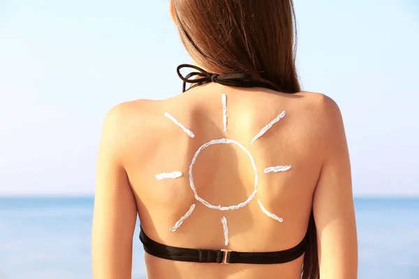 Молода жінка з сонцезахисним кремом на спині, морський фон — стокове фото