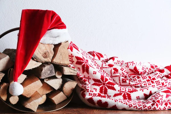 Panier avec bois de chauffage, plaid et chapeau du Père Noël contre le mur blanc — Photo