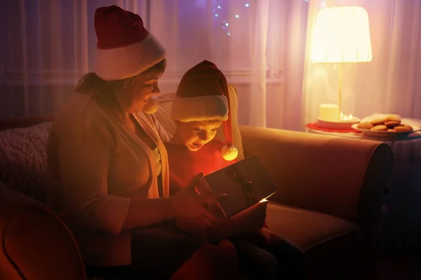 老妇与孙子打开圣诞礼物时坐在客厅里的沙发上 — 图库照片