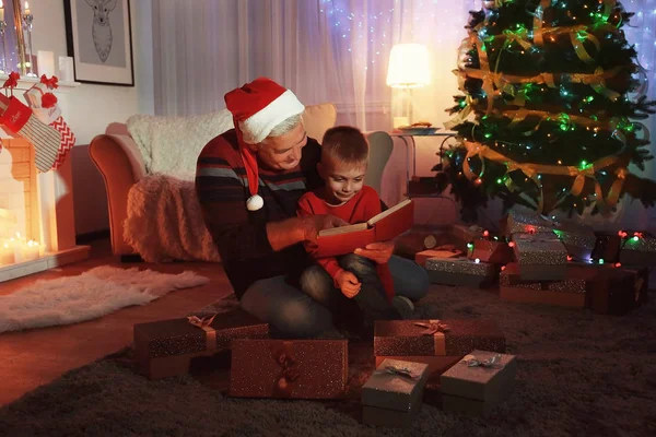 Anciano con nieto leyendo libro en salón decorado para Navidad — Foto de Stock