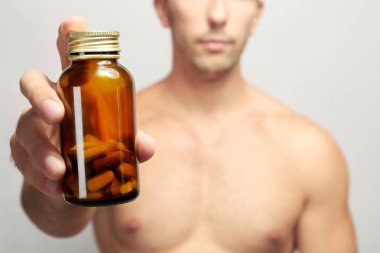 Muscular man holding drugs in bottle, closeup clipart
