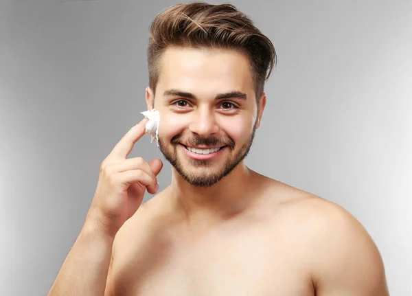 Hombre joven aplicando espuma de afeitar sobre fondo gris —  Fotos de Stock