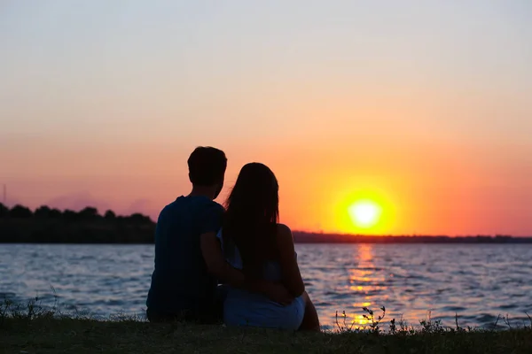 Pasangan muda jatuh cinta duduk dalam pelukan di pantai saat matahari terbenam — Stok Foto