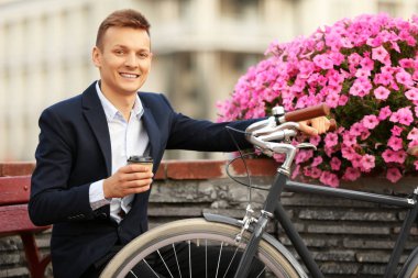 Kahve-to-go kavramı. Bisiklet ve kahve bankta oturan genç adam