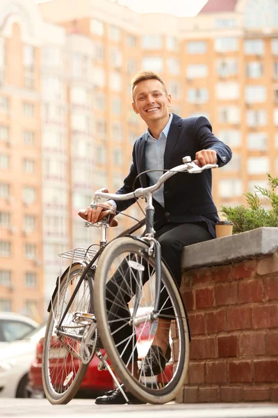 Coffee-to-go concept. Young man with bicycle and cup of coffee on street