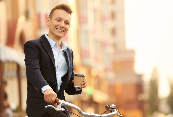 Coffee-to-go concept. Young man with bicycle and cup of coffee on street