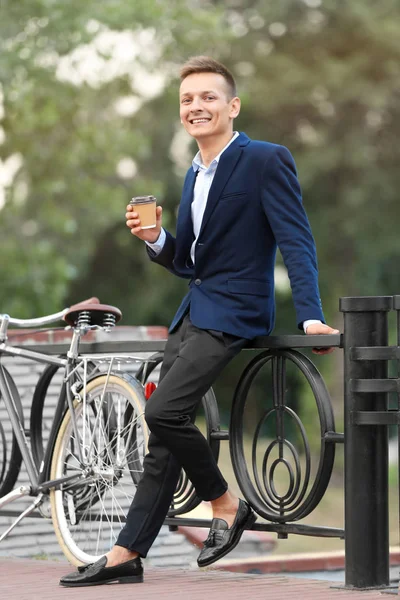 Coffee-to-go concept. Young man with bicycle and cup of coffee on street