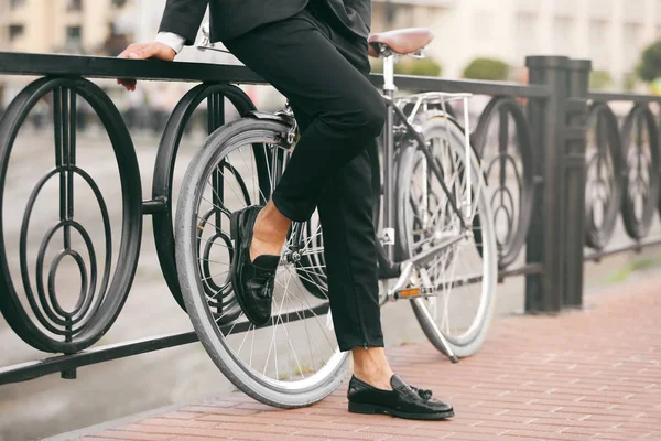 Молодой бизнесмен с велосипедом стоит рядом с перилами на улице — стоковое фото
