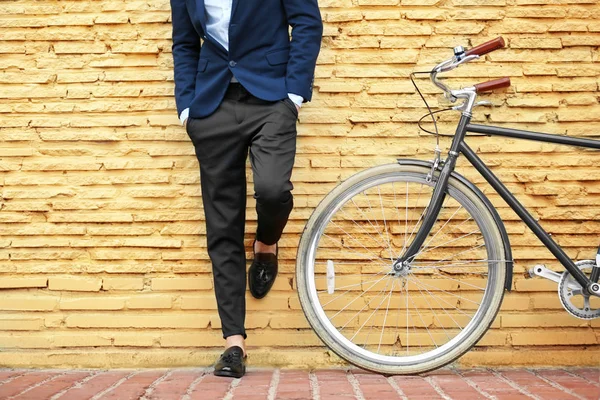 Joven hombre de negocios con bicicleta sobre fondo de pared de ladrillo amarillo —  Fotos de Stock