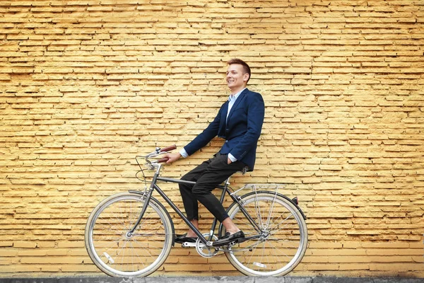 Joven hombre de negocios con bicicleta sobre fondo de pared de ladrillo amarillo —  Fotos de Stock