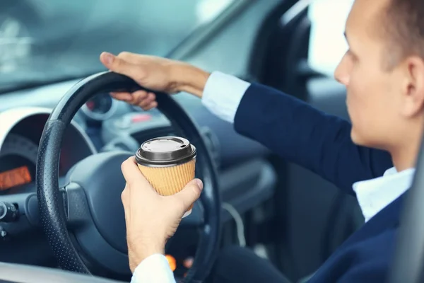 Bonito homem dirigindo um carro e segurando xícara de papel de café — Fotografia de Stock