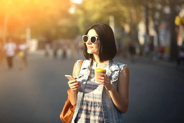 Ung vacker flicka med kopp kaffe och telefonen utomhus — Stockfoto