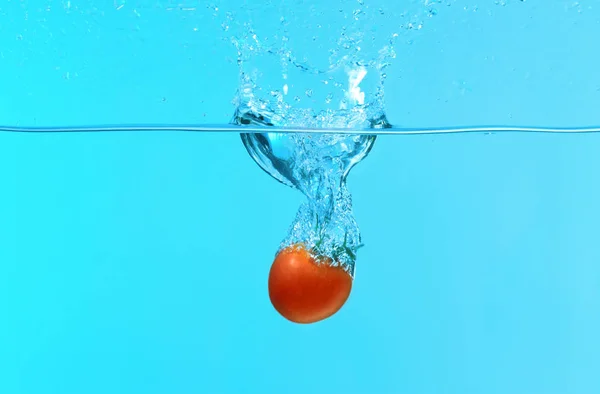 Tomate fällt ins Wasser auf farbigem Hintergrund — Stockfoto