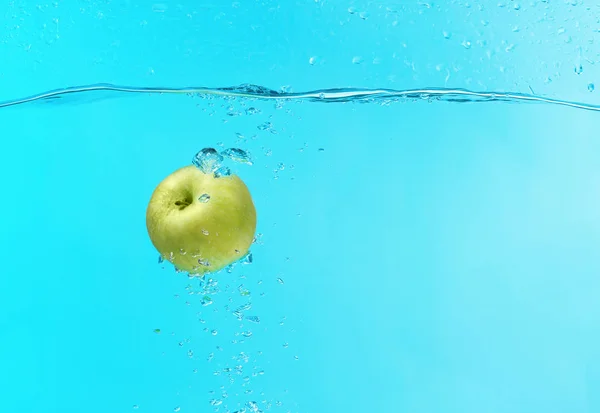 Grönt äpple falla i vatten på färgbakgrund — Stockfoto