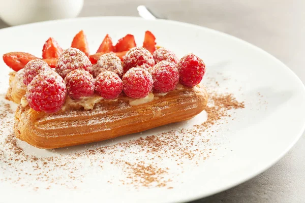 Delicious eclairs with berries, ground cinnamon and sugar powder on white plate — Stock Photo, Image