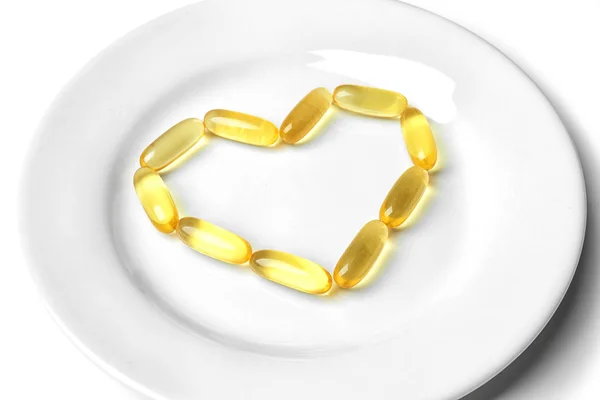 Fish oil pills in heart shape on plate, close up — Stock Photo, Image