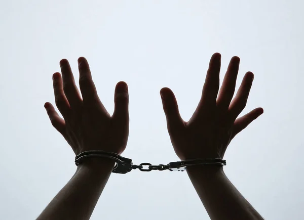 Black silhouette of man hands in handcuffs on light background — Stock Photo, Image