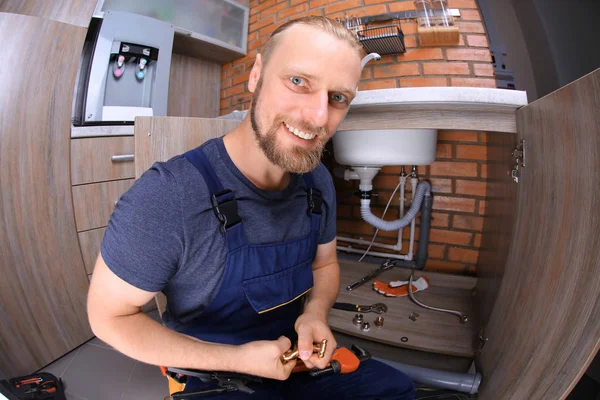 Funny fontanero reparar tuberías de fregadero en la cocina —  Fotos de Stock