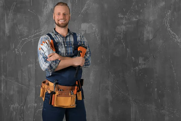 Handsome plumber with pipe wrench and gloves on grunge background — Stock Photo, Image