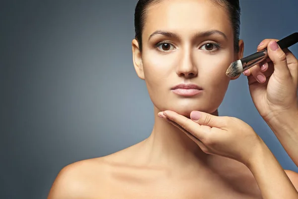 Menina bonita aplicando cosméticos no fundo cinza — Fotografia de Stock