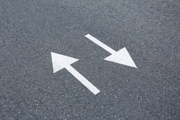 Arrow signs on asphalt road showing direction of movement, close up