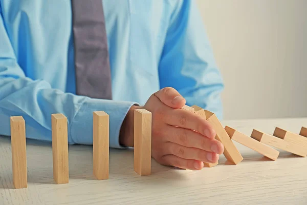 Geschäftsmann Hand versucht, das Umfallen von Dominosteinen auf dem Tisch zu stoppen — Stockfoto