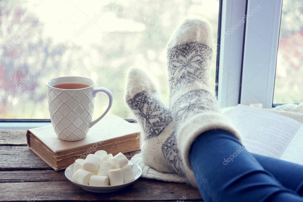 Female legs and hot drink with marshmallows on windowsill